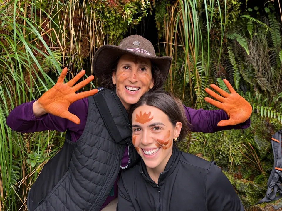 Ana Mercedes y Francesca sonriendo en la montaña, con las manos y el rostro pintados para el ritual